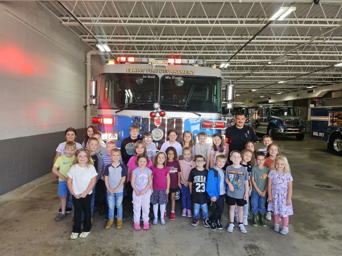 Students posing with firefighters in front of a fire truck during a field trip to the fire station