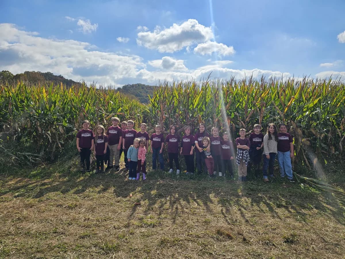 Students wearing school shirts posing in front of a cornfield during fall field trip