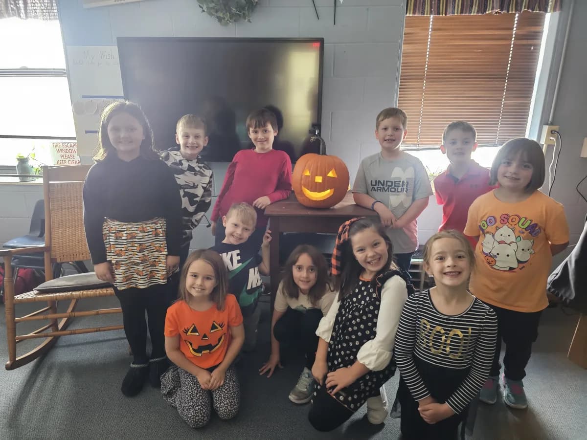 Students posing with a carved jack-o-lantern during fall classroom celebration