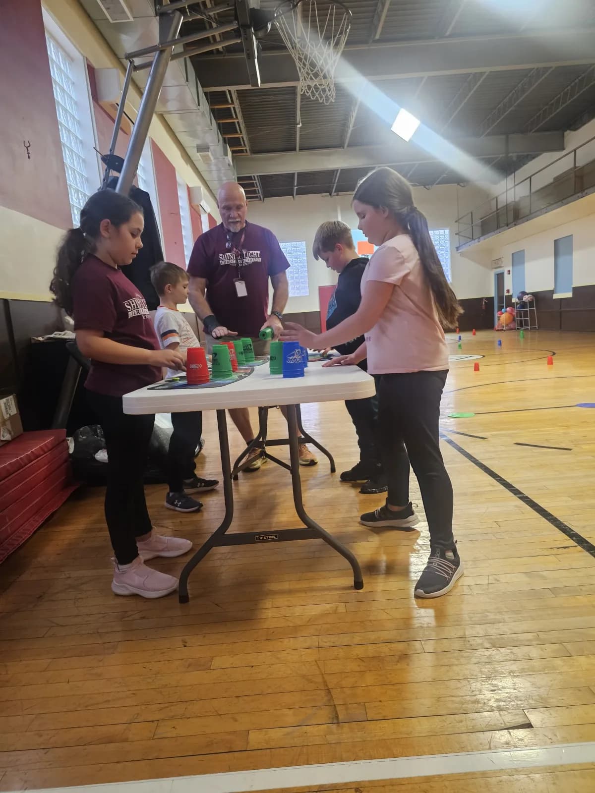 Students practicing cup stacking at a table during PE class
